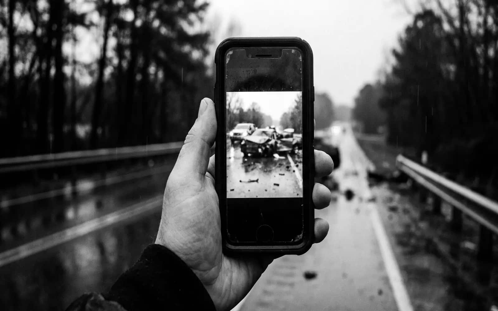 Hand holding a phone at roadside showing a photo of a crash scene